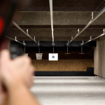 Foto de um atirador com uma arma, mirando no alvo, em um estande de tiro