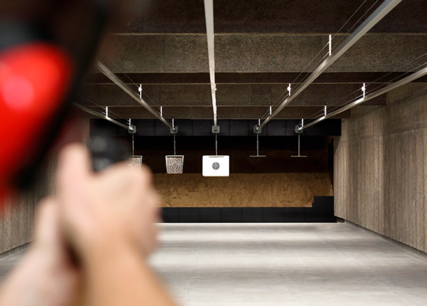 Foto de um atirador com uma arma, mirando no alvo, em um estande de tiro