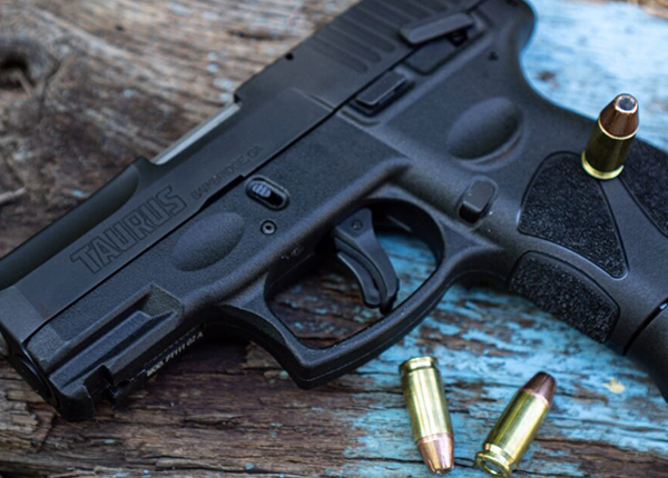Uma pistola Taurus G2C e munições calibre 9mm em cima de uma mesa de madeira
