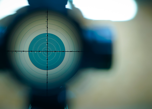 Foto de um alvo de precisão na mira de uma arma, com o cano em close up e fundo desfocado